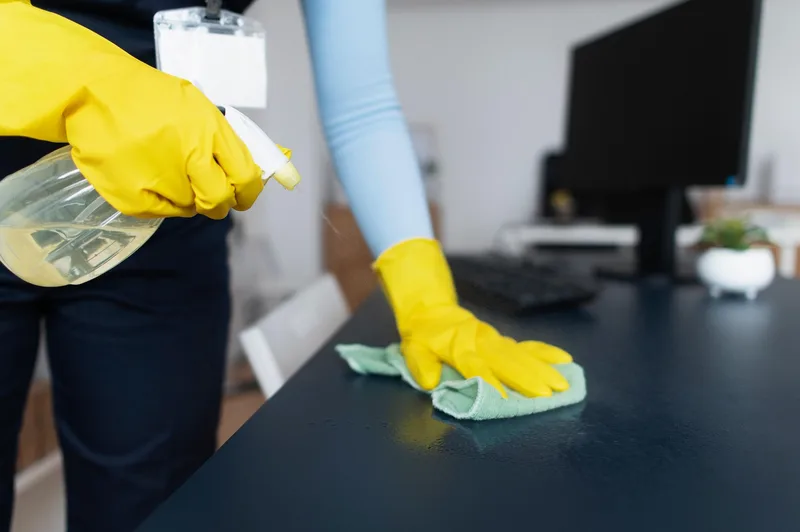 Main gantée de jaune qui essuie une surface avec un chiffon vert après avoir pulvérisé un produit