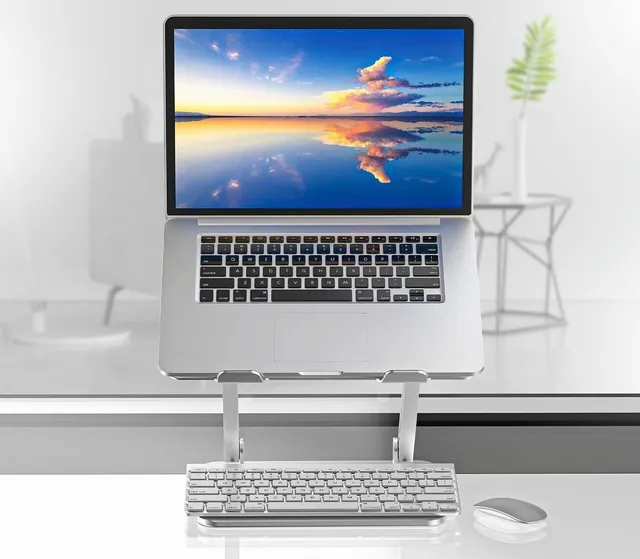 Ordinateur portable sur un support en aluminium, avec un clavier et une souris sans fil rangés sous la plateforme