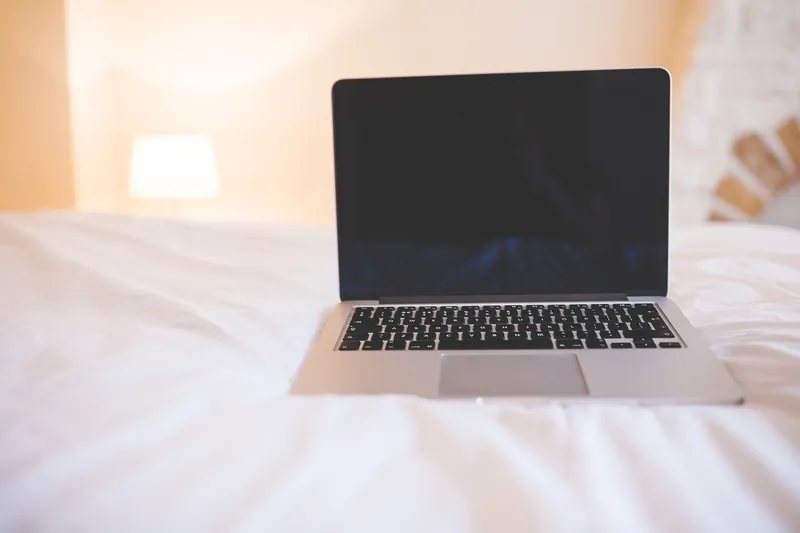 Ordinateur portable ouvert, posé sur une couette blanche dans une chambre